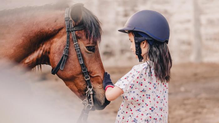Kind mit Reithelm streichelt Pferd beim Therapeutisches Reiten für Kinder