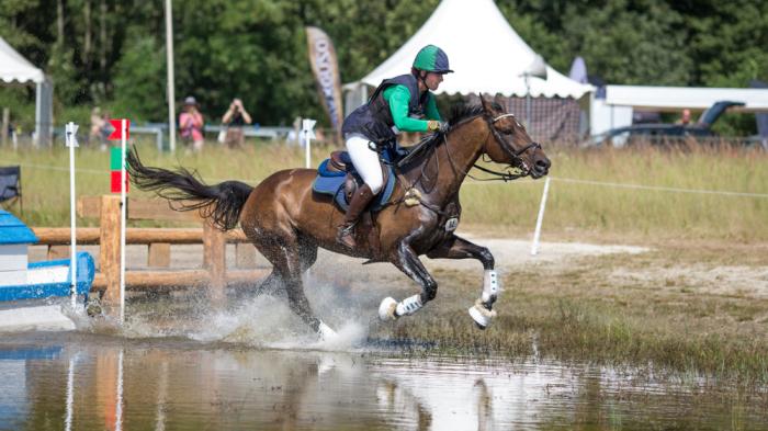 Reiter reitet auf Pferd durch Wasserhindernis beim Vielseitigkeitsreiten