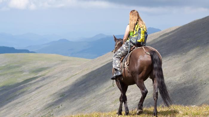 Reiterin auf Pferd beim Wanderreiten in den Bergen