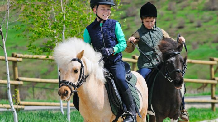 Zwei Kinder Reiten Ponys während Reiterferien für Kinder