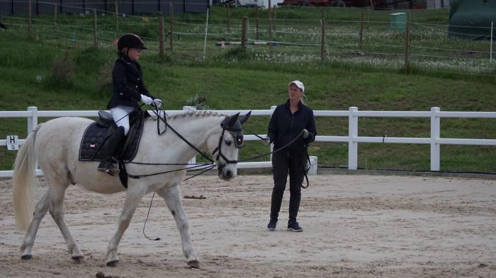 Kind auf weißem Pferd an Longe auf Reitplatz.jpg