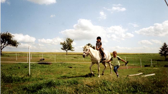 Ein Mädchen rennt mit einem einem weißen Pony am Strick über eine Wiese