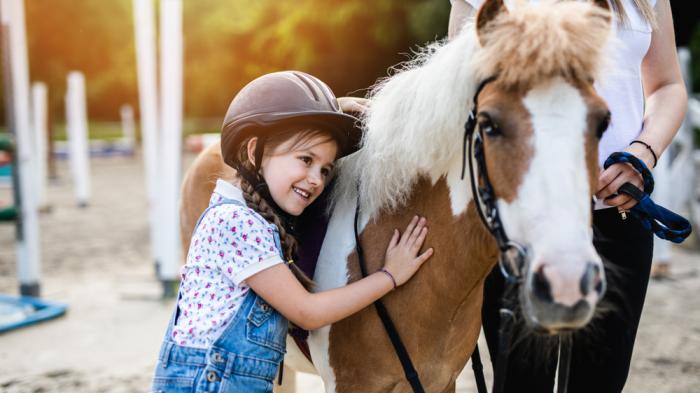 Ein Pferdemädchen mit Reitkappe lehnt sich an ein braun-weißes Pferd