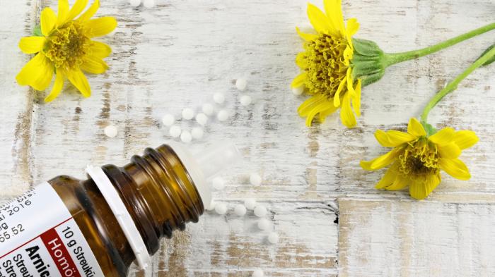 Braune Flasche mit Globulis auf weißem Tisch mit gelben Blumen