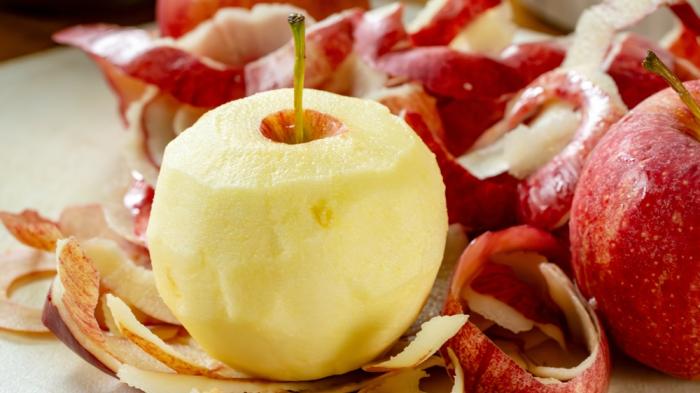 2 rote Äpfel und ein geschälter Apfel, die Schale liegt daneben 