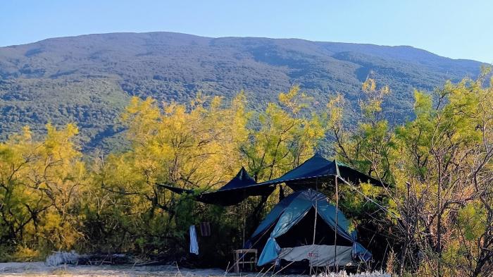 Zelt mit Schattennetz von Bäumen umgeben und im Hintergrund ist ein Berg