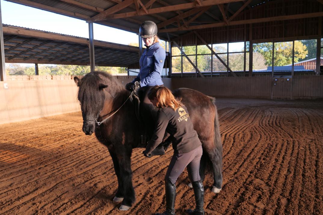 Reitlehrerin hilft Reiterin auf braunem Pferd mit den Steigbügeln beim Reitunterricht für Erwachsene