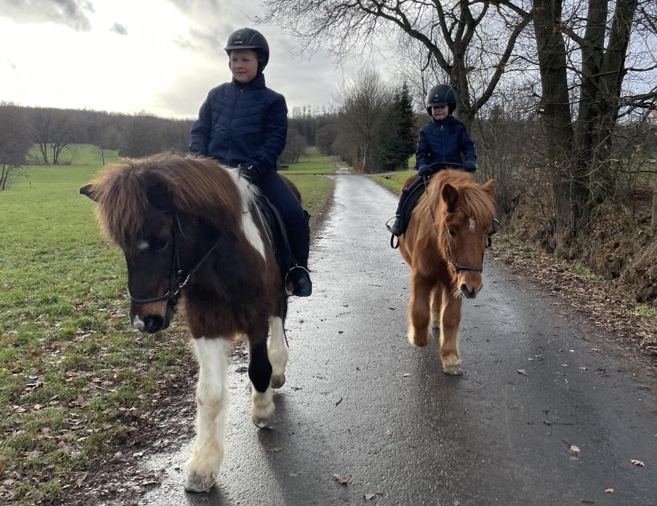 Reiten lernen für Kinder: Zwei Kinder auf Ponys beim Ausreiten im Gelände