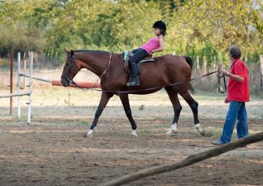 Kind macht Übungen auf Pferd während der Hippotherapie mit Therapeutin