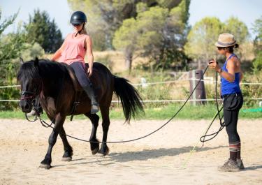 Kind reitet freihändig auf Pferd beim Therapeutischen Reiten mit Reitlehrerin