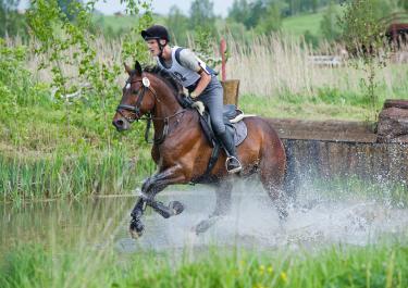 Reiter auf Pferd galoppiert im Wassserhinderniss beim Vielseitigkeitsreiten