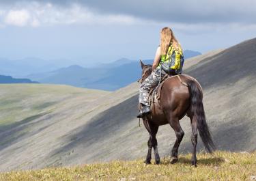 Reiterin auf Pferd beim Wanderreiten in den Bergen