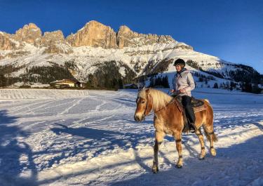 Reiterin auf Pferd reitet durch verschneite Berglandschaft